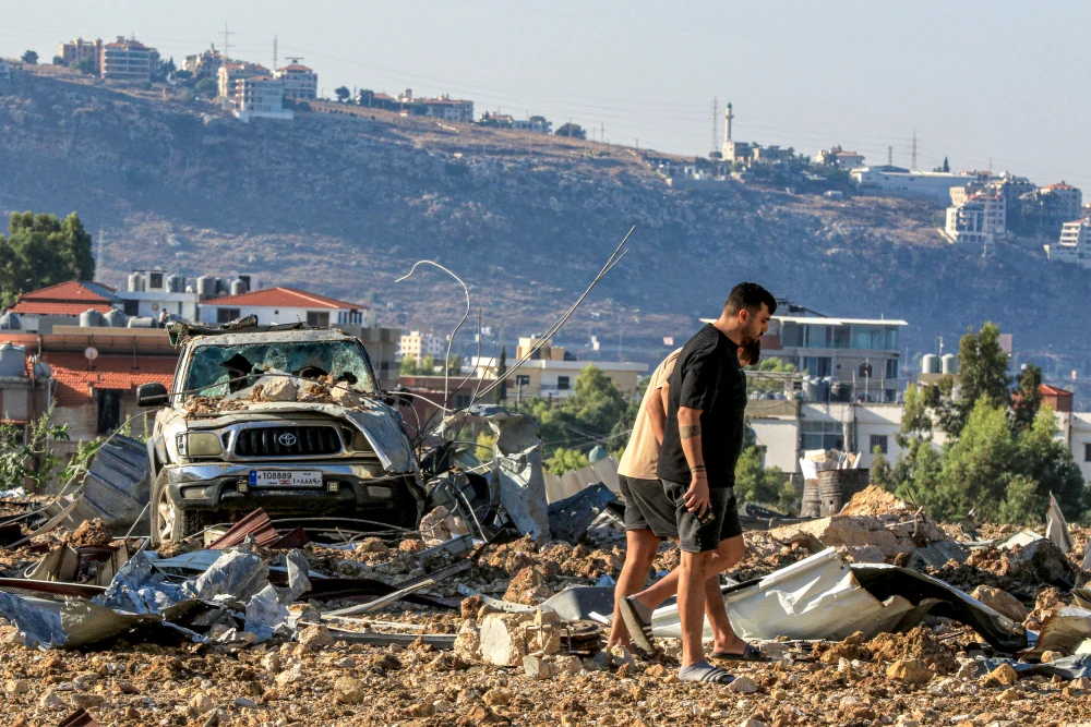 Dua orang berada di sekitar reruntuhan pasca serangan Israel di Lebanon.